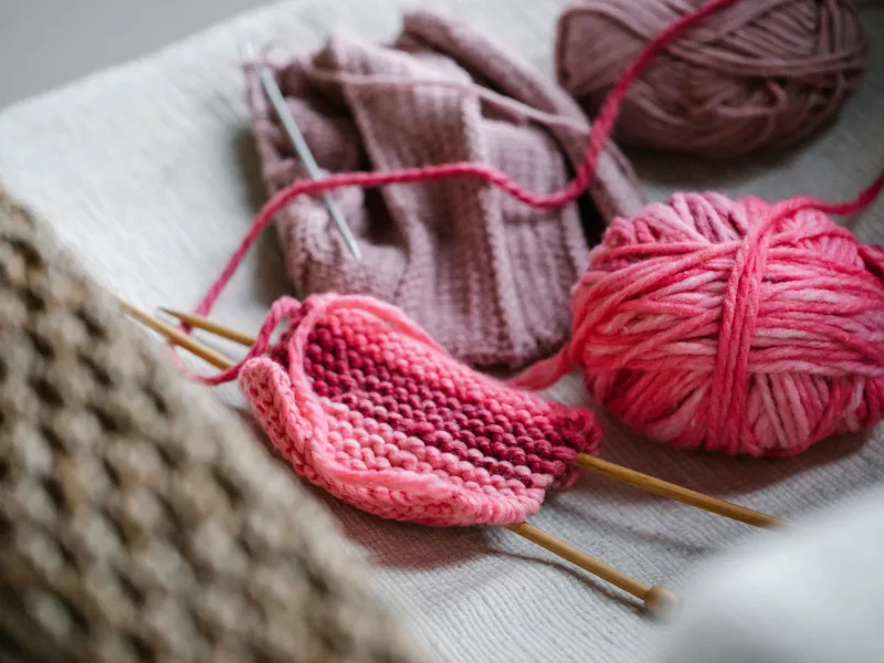 Two balls of pink knitting wool with knitting needles