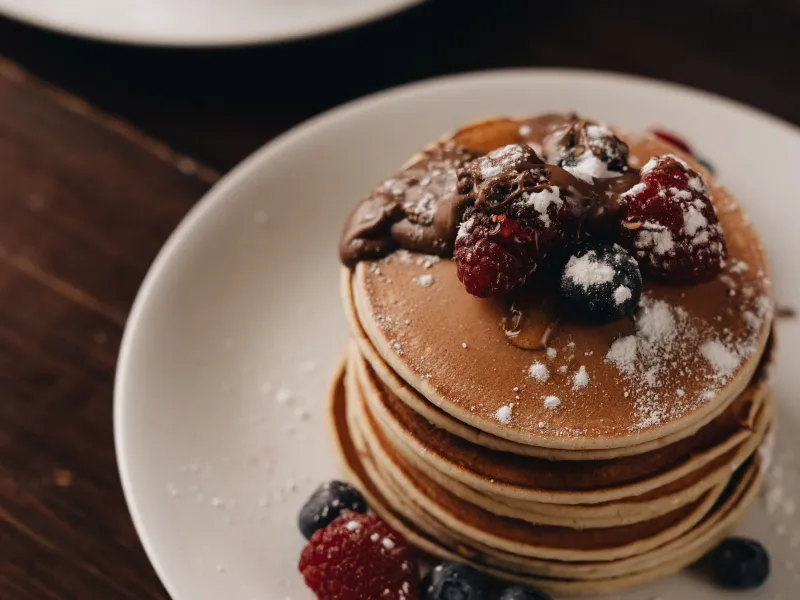 A stack of pancakes topped with mixed berries and chocolate