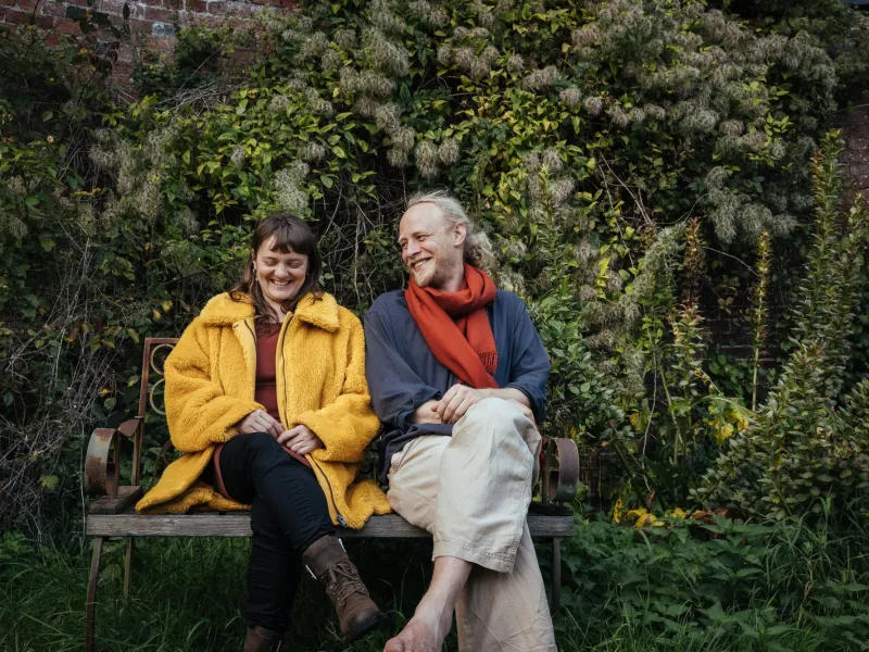 A woman in yellow anorak next to a man on a bench