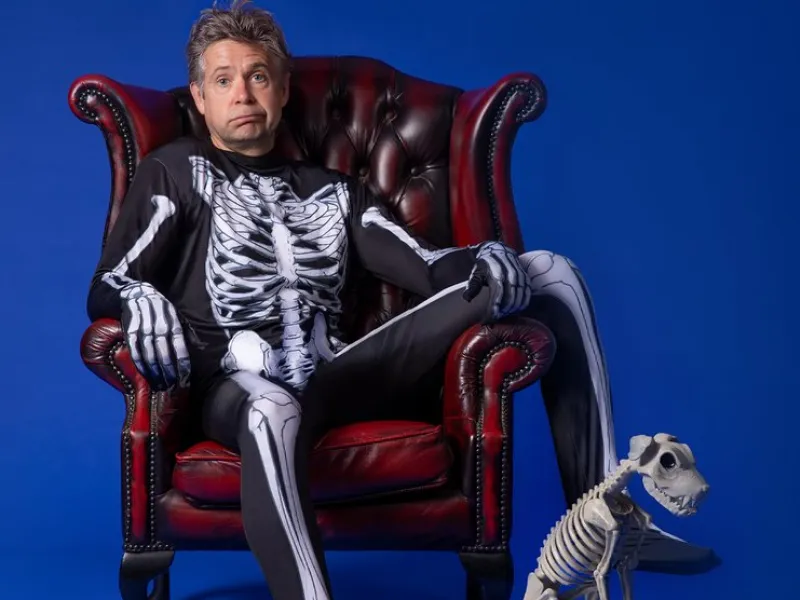 The comedian Rob Rouse in a red armchair wearing a skeleton jumpsuit