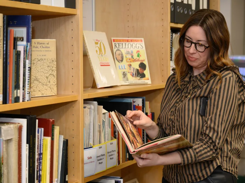 A woman looking at a book next to some bookshelves
