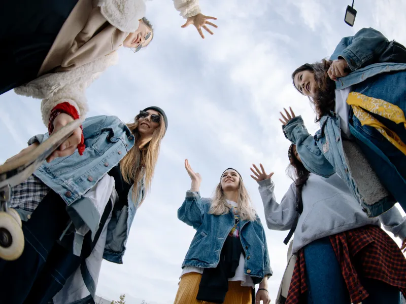 Women stood in a circle waving to each other with a blue sky behind them