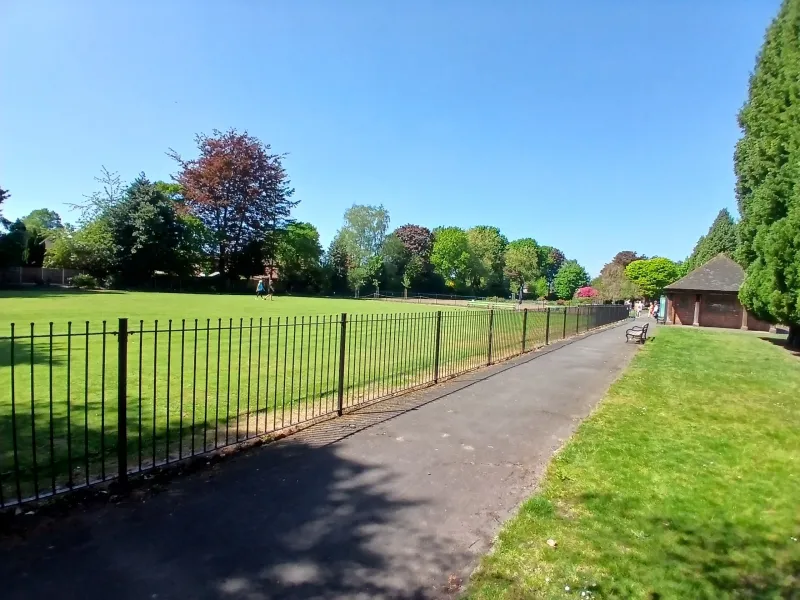 A path through a park next to some railings, with trees in the distance