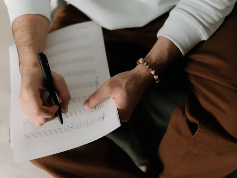 Hands holding a pen and sheet music, seen from above