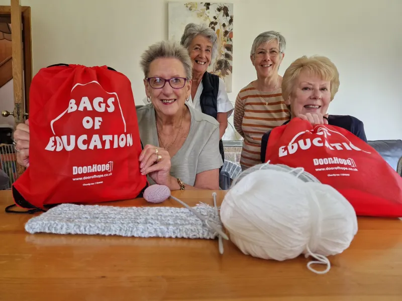 Women with some knitting that they have done and red 'bags for education' in front of them