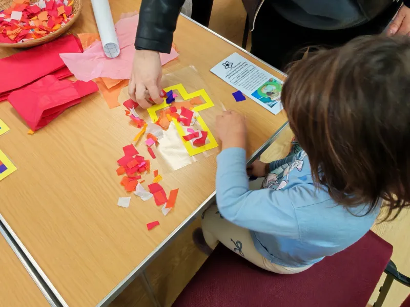 A child creating a stained glass cross with tissue paper