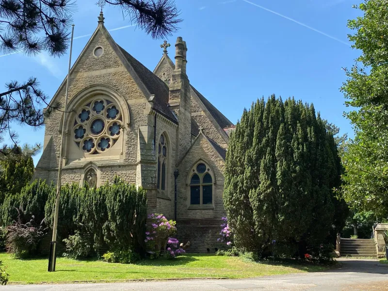 Photo of St John's church as seen from Brooklands Road, showing the church surrounded by trees and shrubs.