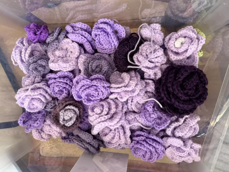 Multiple purple crochet roses, in many shades, in a plastic storage box 