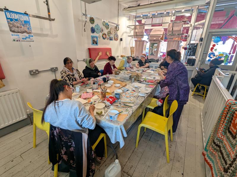 A group of people sat around a table in the OT creative space studio making clay dishes and chatting. 