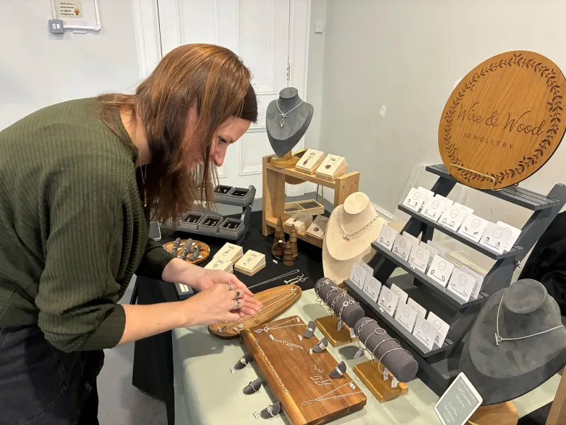 A woman standing over her set up table , arranging silver jewellery 