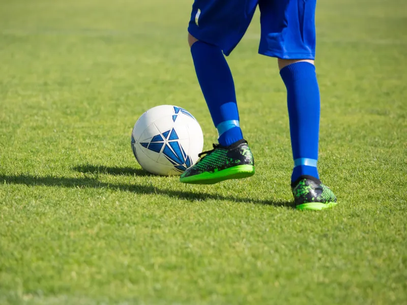 A person wearing a football kit kicking a white football on grass
