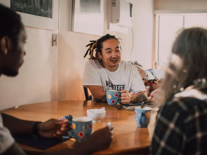 Three people sat talking at a table with coffee mugs