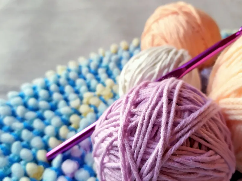 Bundles of knitting yarn and a crochet hook on a blue throw