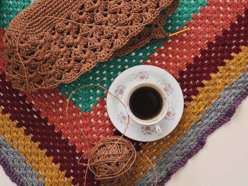 Warm and inviting scene of a crochet project with a cup of coffee on a vibrant, handmade blanket.