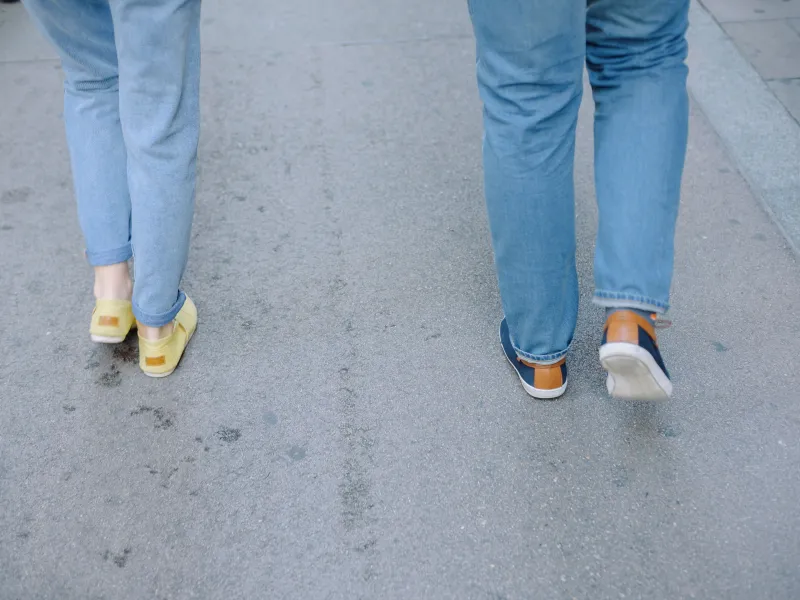 Two people walking on pavement wearing jeans and trainers